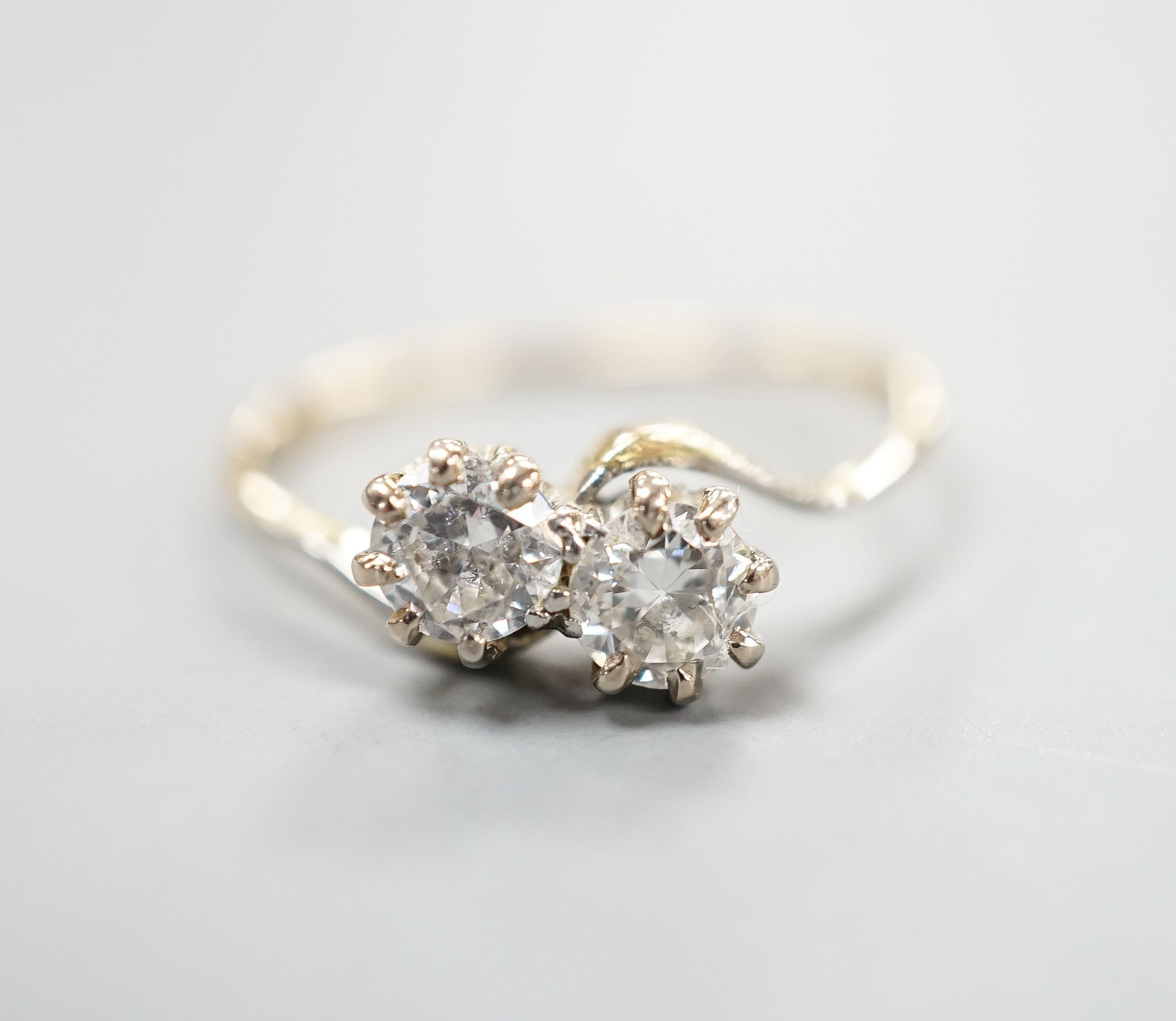 A yellow metal and two stone diamond set crossover ring, size P/Q, gross weight 1.9 grams.